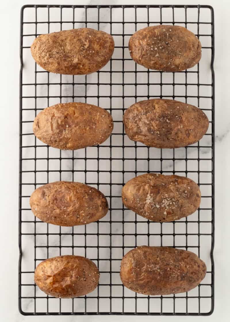 Cooked whole potatoes on a wire rack.