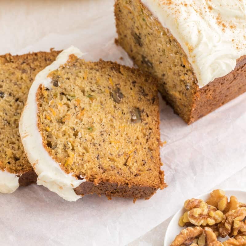 Sliced Carrot Cake Banana Bread on a table next to a bowl of walnuts.