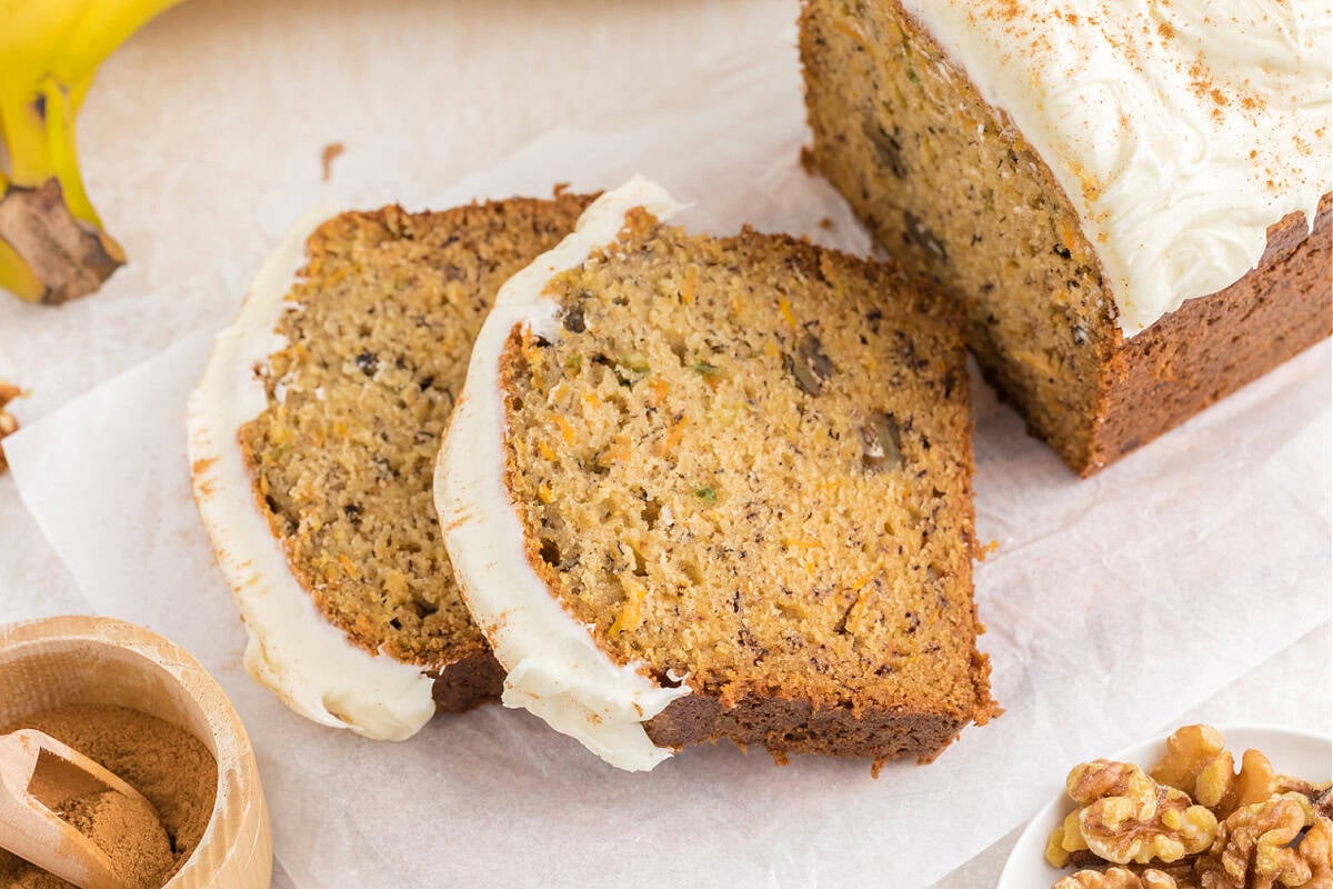 Sliced Carrot Cake Banana Bread on a table next to bananas and chopped walnuts.