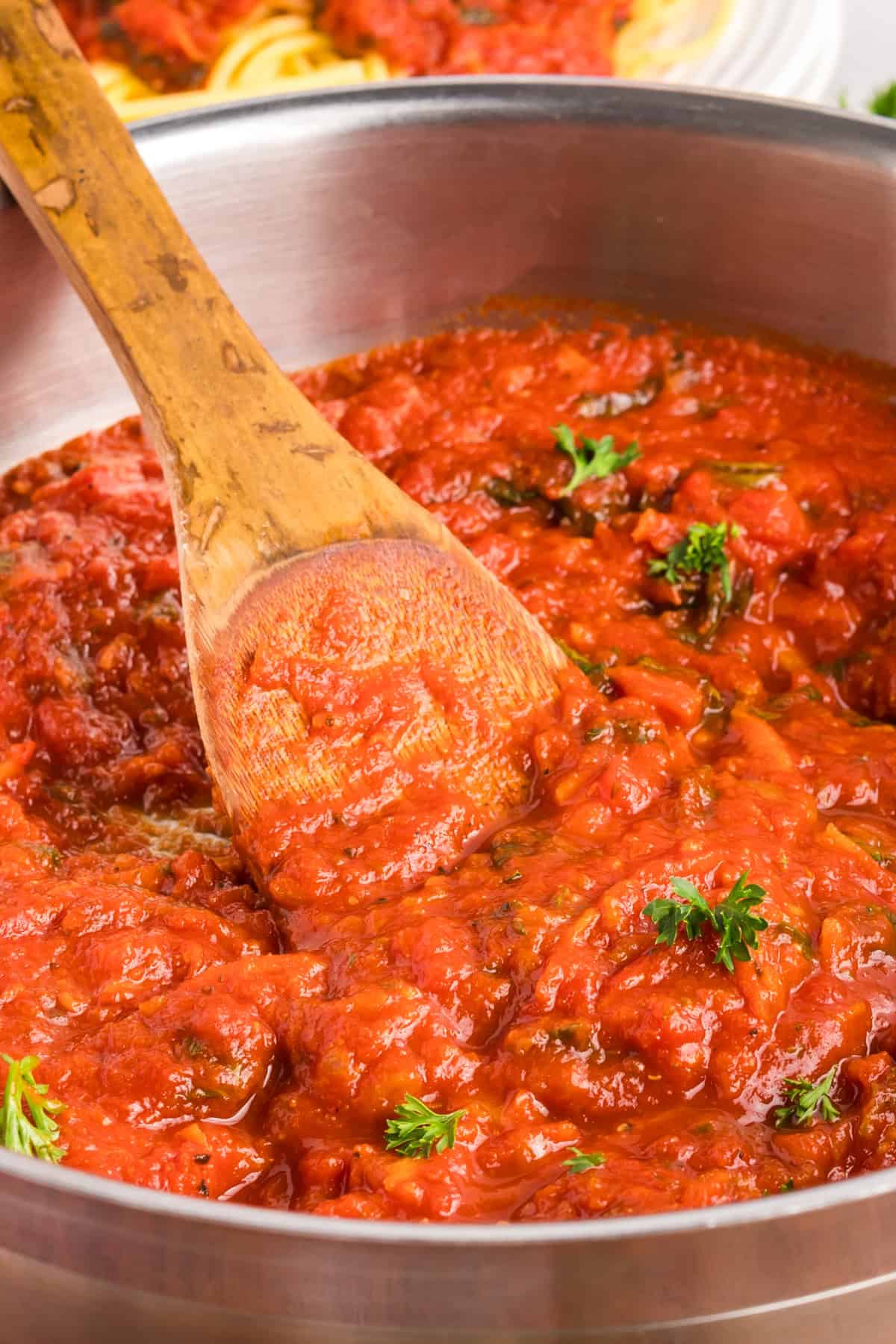 A wooden spoon stirring homemade spaghetti sauce in a large pot.