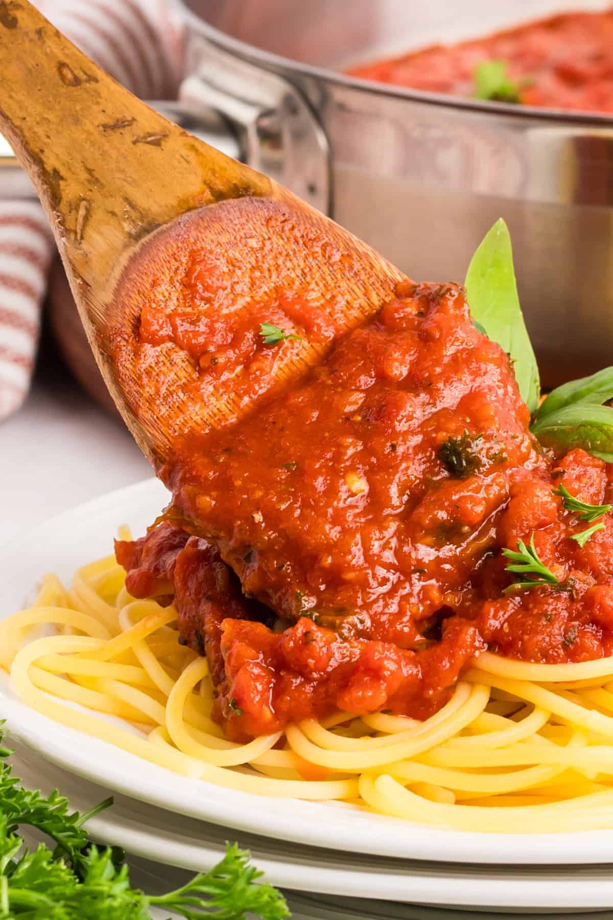 Homemade pasta sauce being added to cooked spaghetti with a wooden spoon.