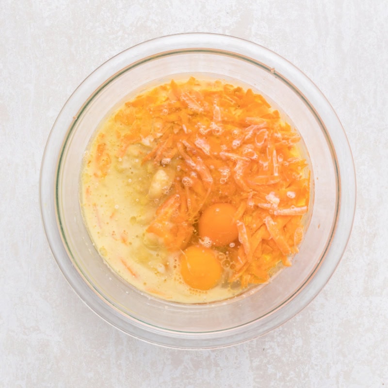 Mashed banana, shredded carrot and eggs in a glass bowl.