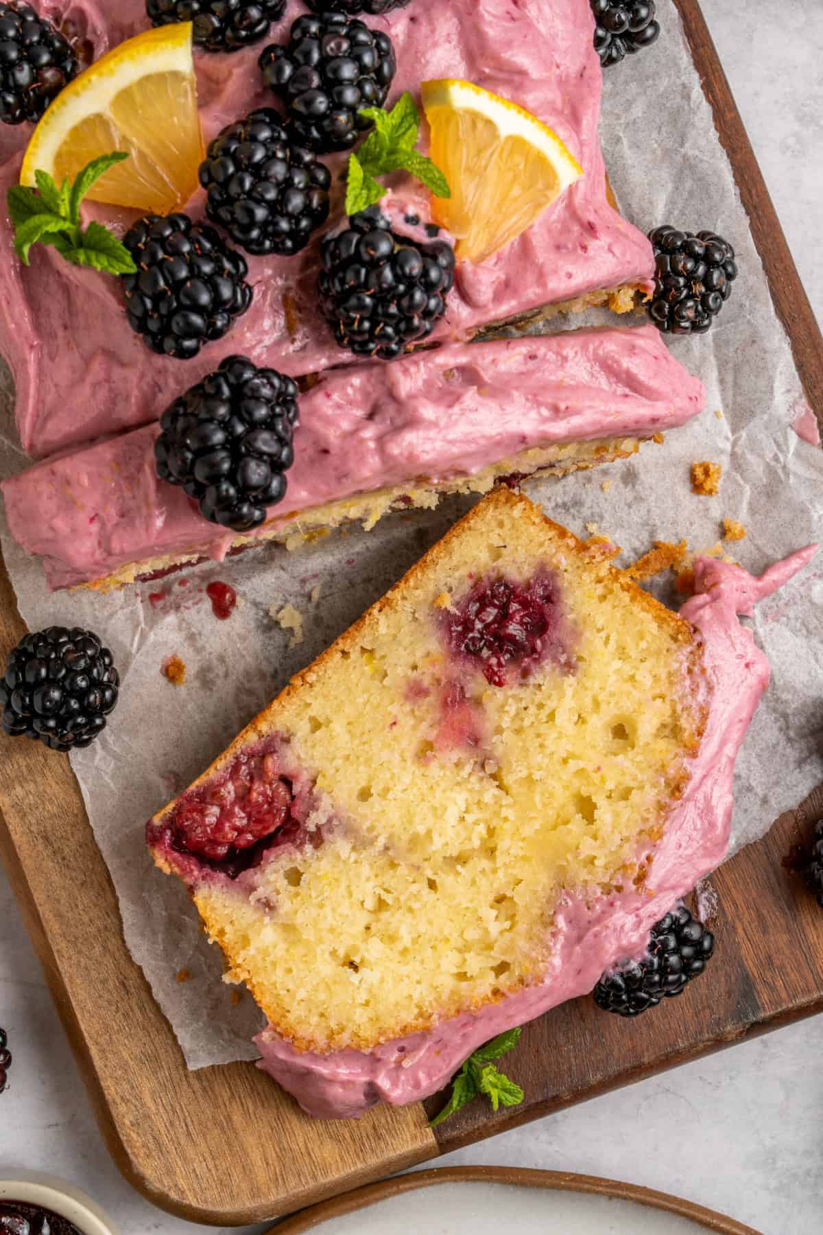Sliced glazed Blackberry Lemon Loaf on parchment paper with fresh blackberries on top.