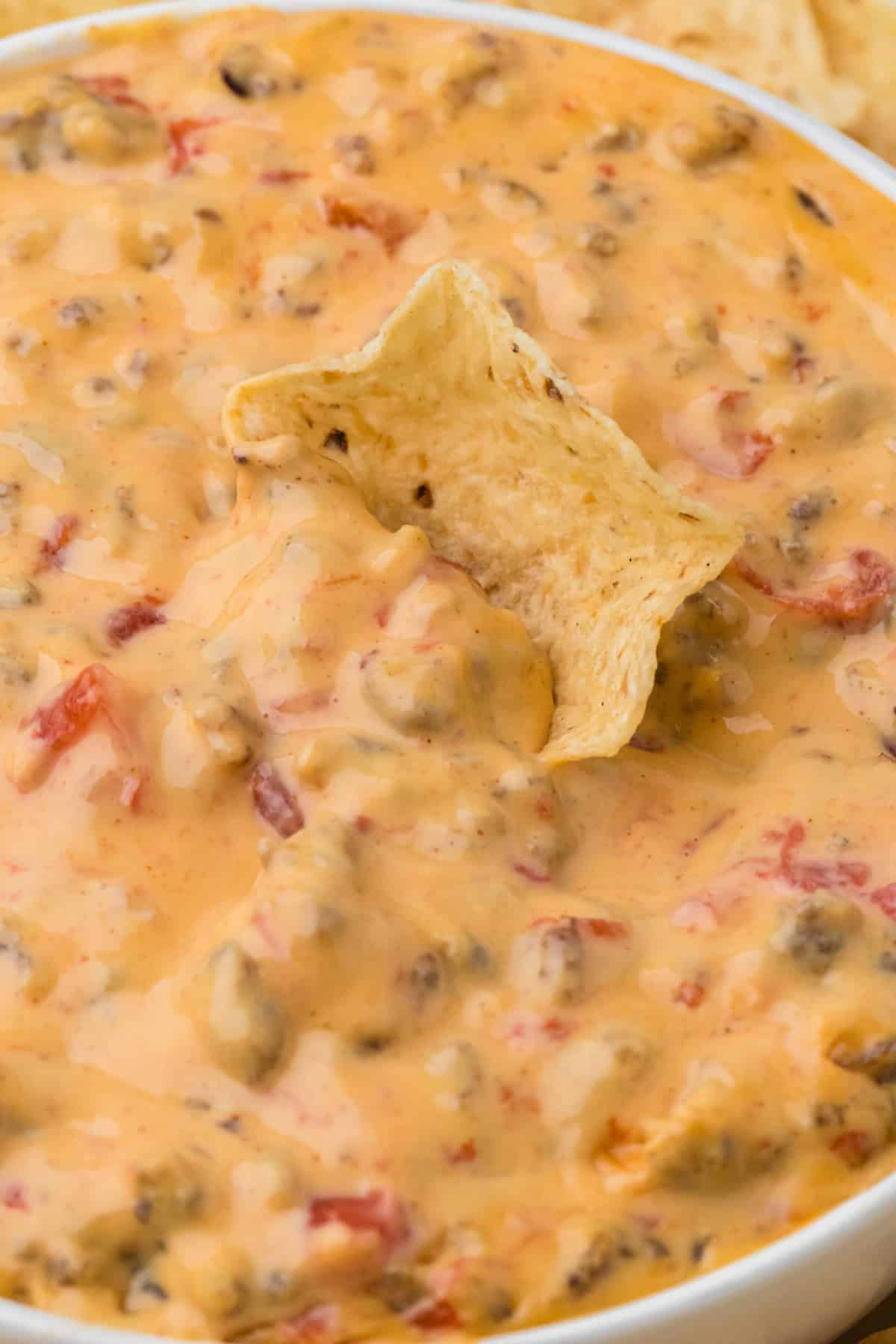 A tortilla chip being dipped into Rotel Cheese Dip.