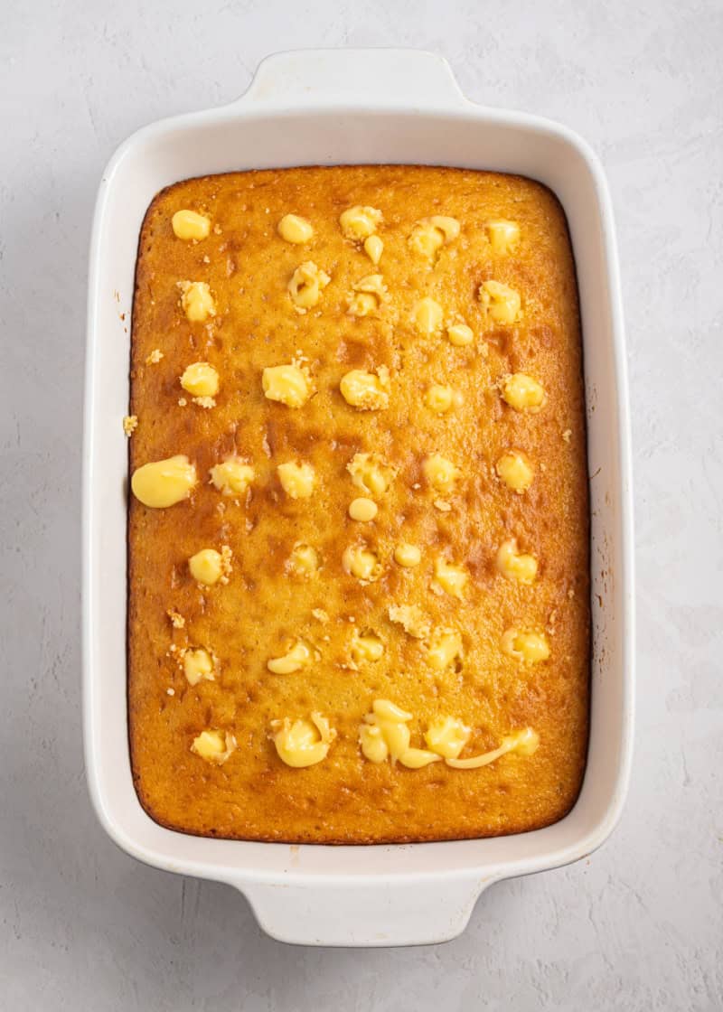 A whole baked yellow cake with holes poked into it with pineapple pudding inside the holes.