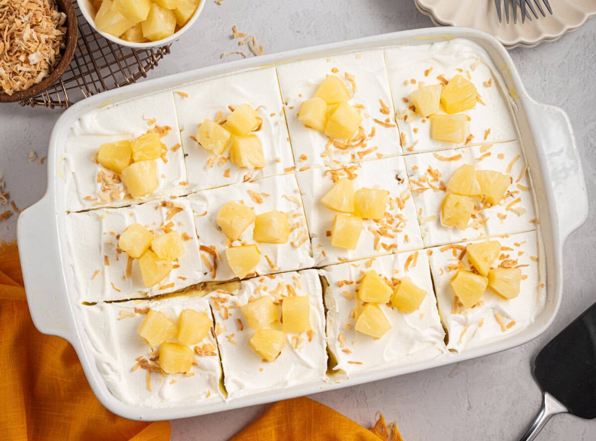 A whole sliced Pineapple Poke Cake with cool whip, pineapple chunks and toasted coconut on top.