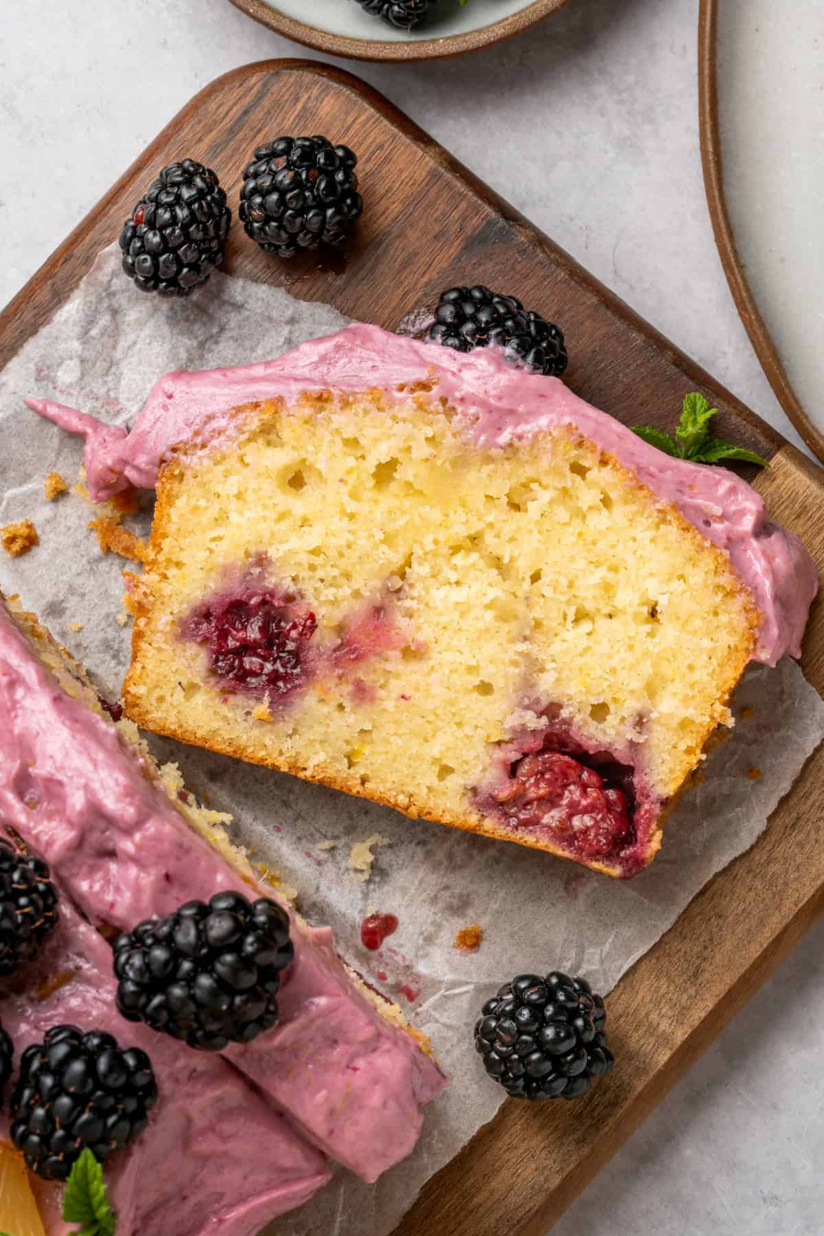 Sliced glazed Blackberry Lemon Loaf on parchment paper with fresh blackberries on top.