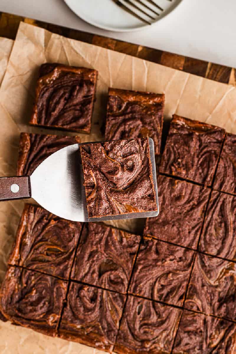 A Mexican brownie swirled with dulce de leche being lifted from many using a spatula.