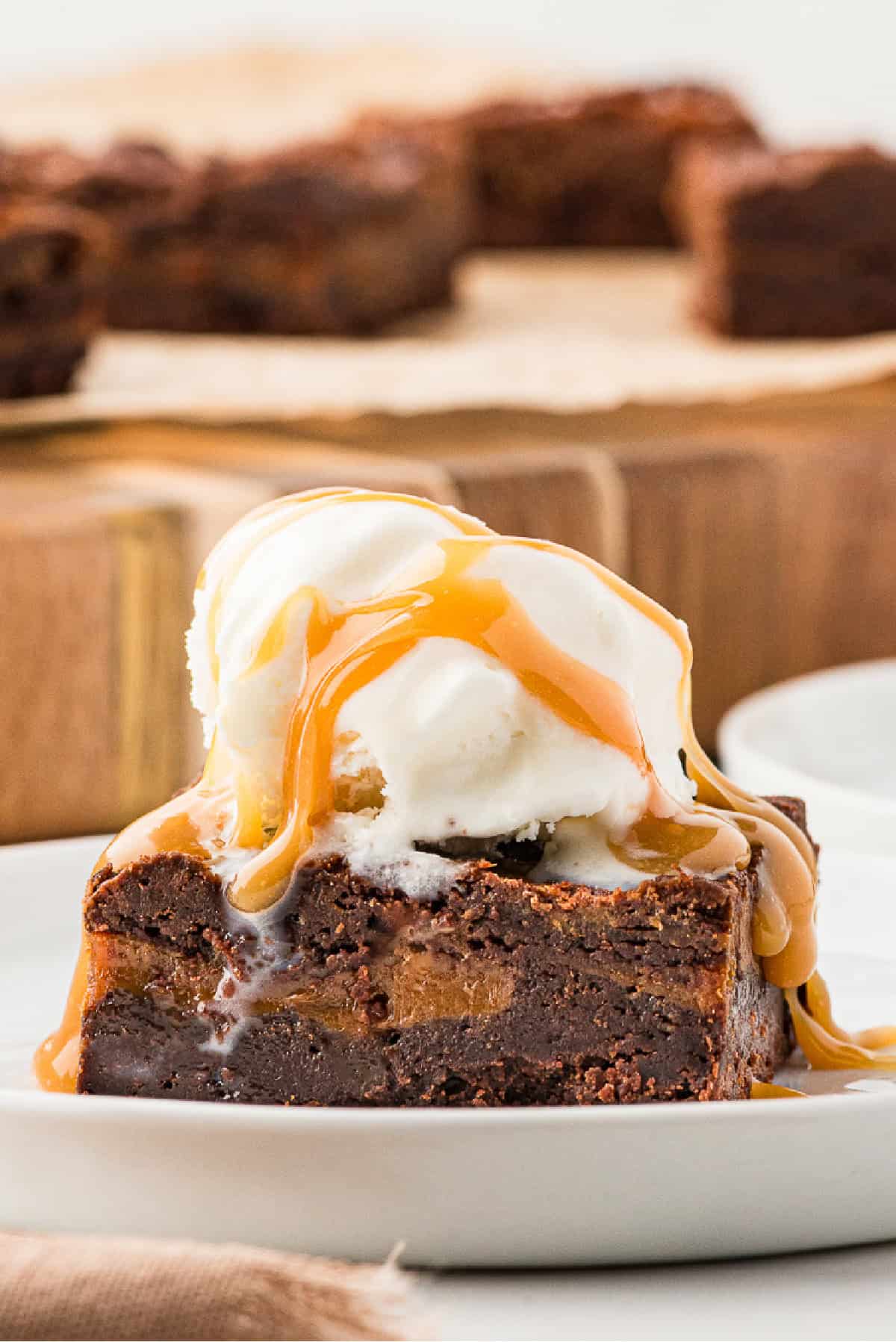 Mexican brownie swirled with dulce de leche on a white plate with ice cream on top drizzled with caramel sauce.
