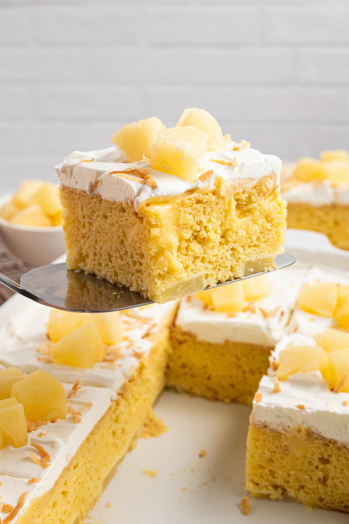 A slice of Pineapple Poke Cake being lifted from the entire cake.