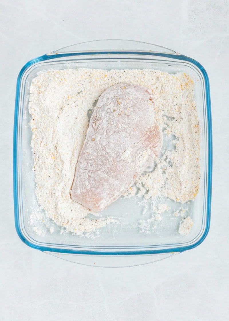 flour coating chicken breast sin a glass dish.