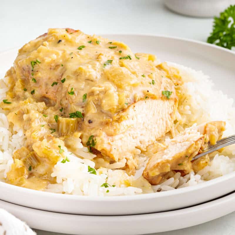 A fork taking a piece of smothered chicken on a plate with rice.