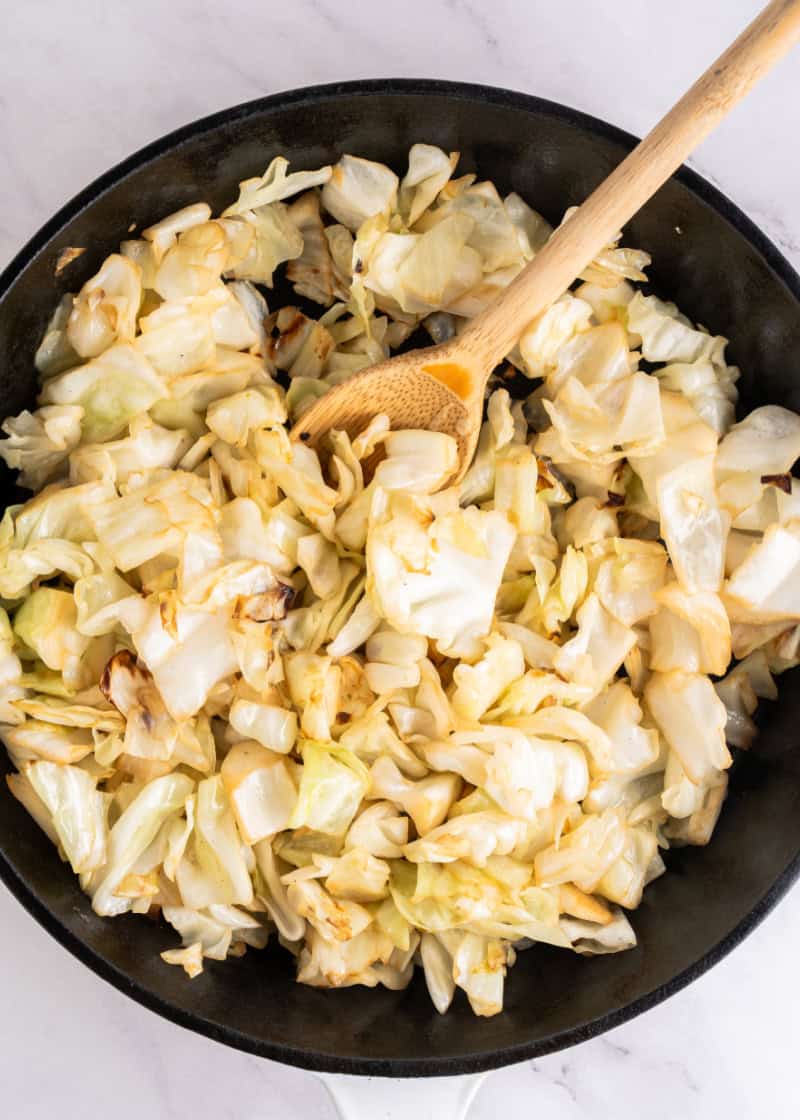 cooking chopped cabbage in a pan with a wooden spoon.
