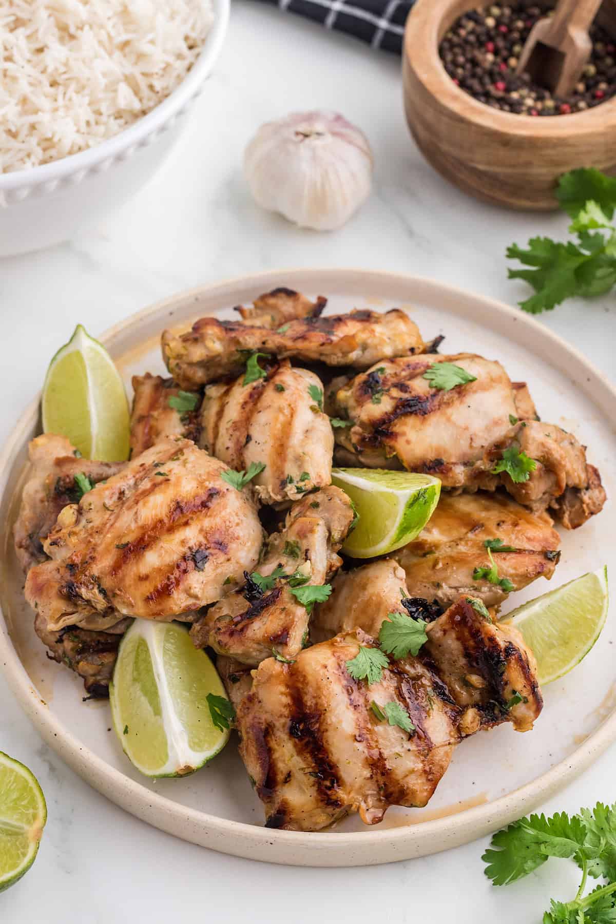 Thai BBQ Chicken on a white plate with lime wedges and a side of rice.