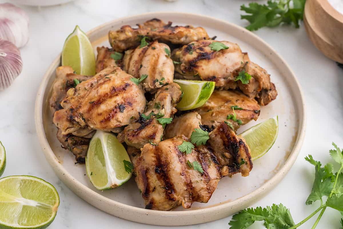 Thai BBQ Chicken on a plate with lime wedges and cilantro.