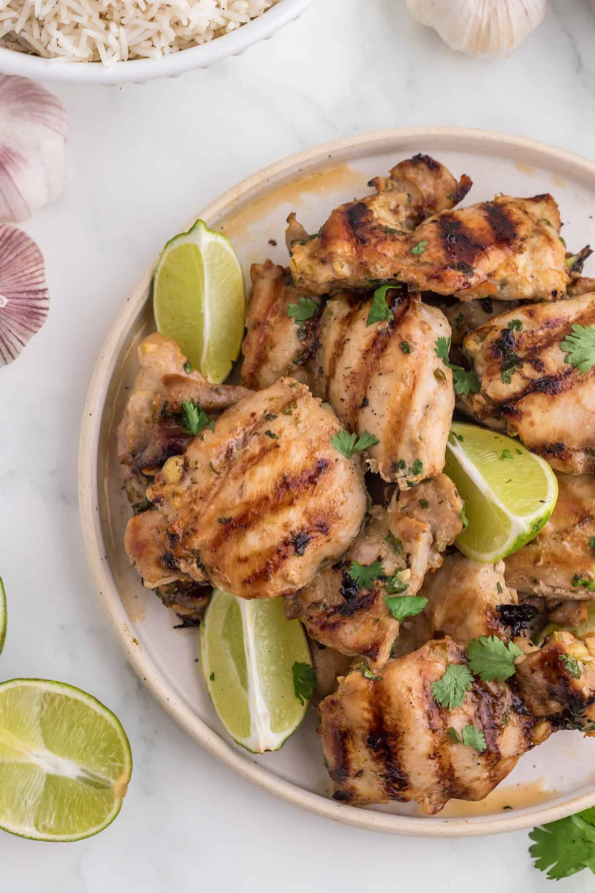 Thai BBQ Chicken on a white plate with lime wedges, fresh cilantro and a side of cooked rice.