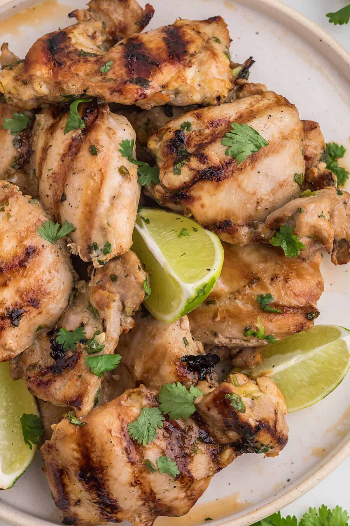 Marinated and cooked Thai BBQ Chicken on a round white plate with lime slices.