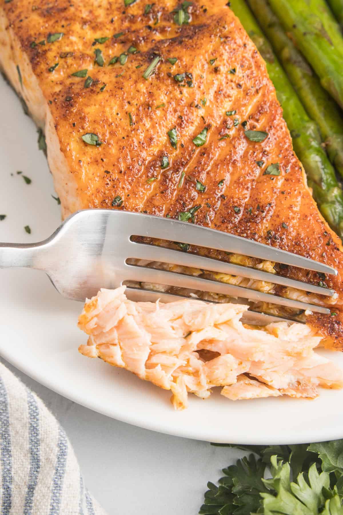 A piece of salmon with a fork and a side of asparagus.