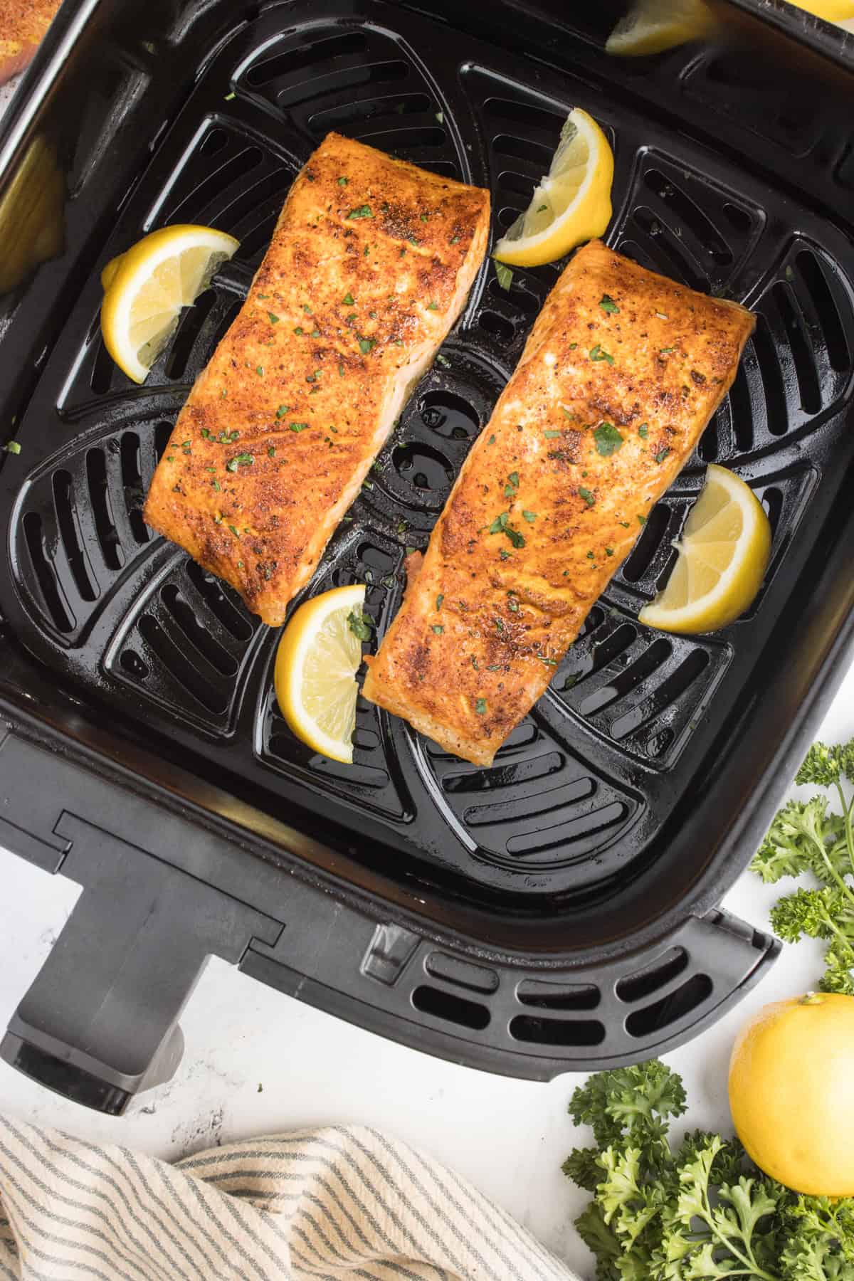 Salmon in an air fryer basket with slices of lemon.