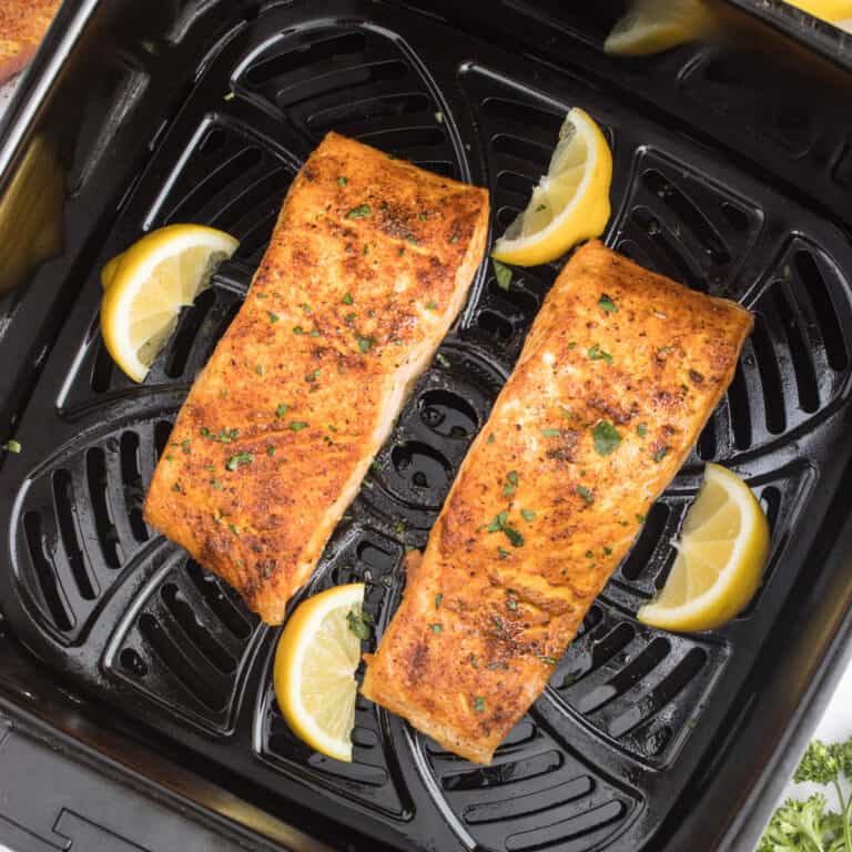 Cooked salmon fillets in an air fryer with lemon wedges.