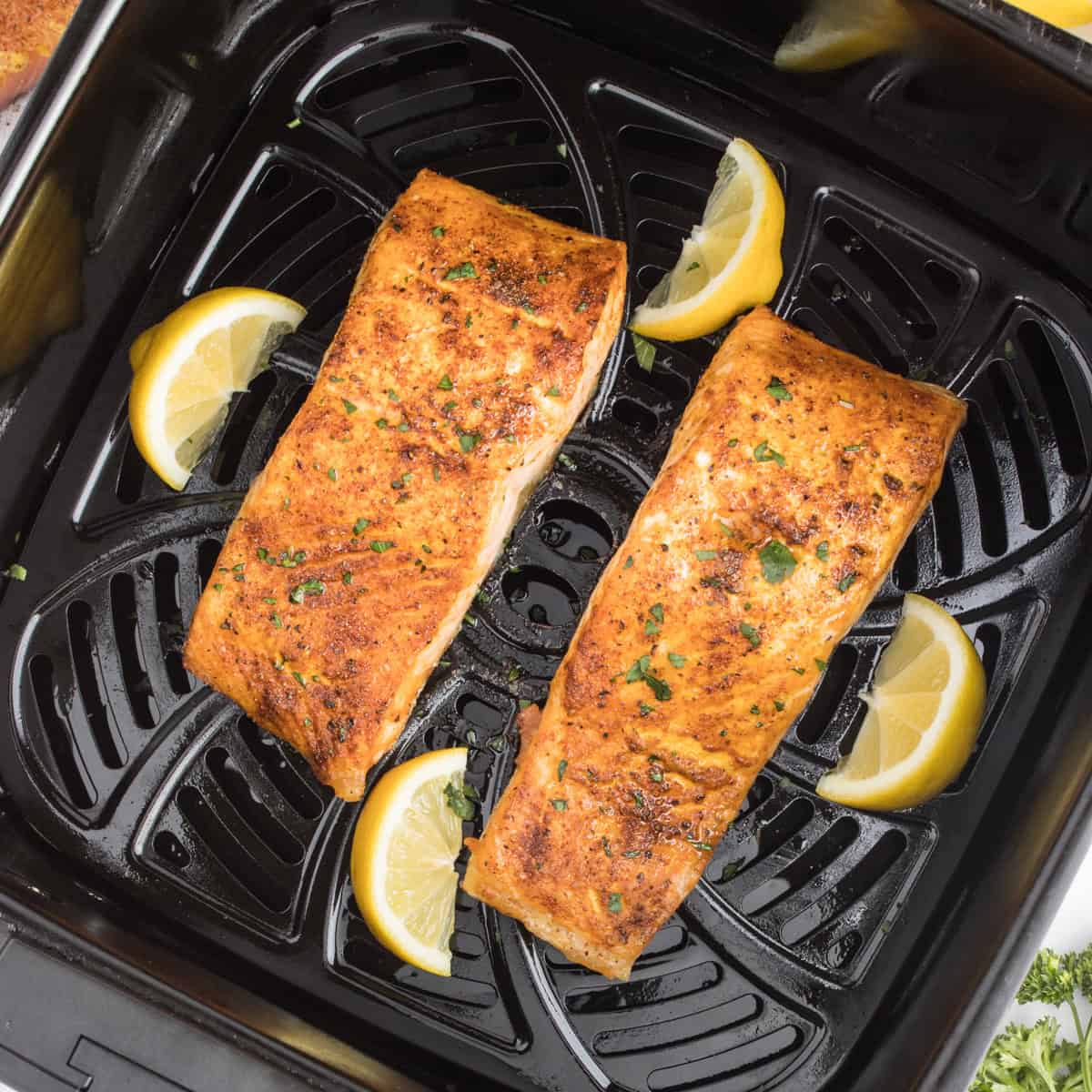 Cooked salmon fillets in an air fryer with lemon wedges.