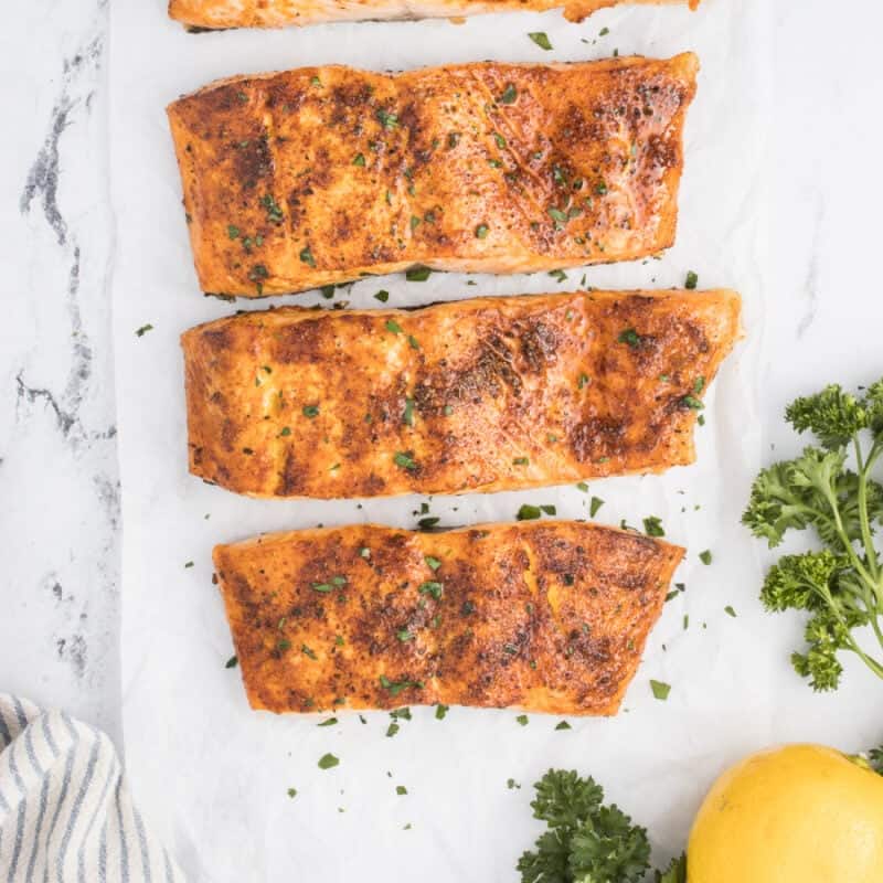 Cooked salmon fillets in a table with fresh parsley on top.