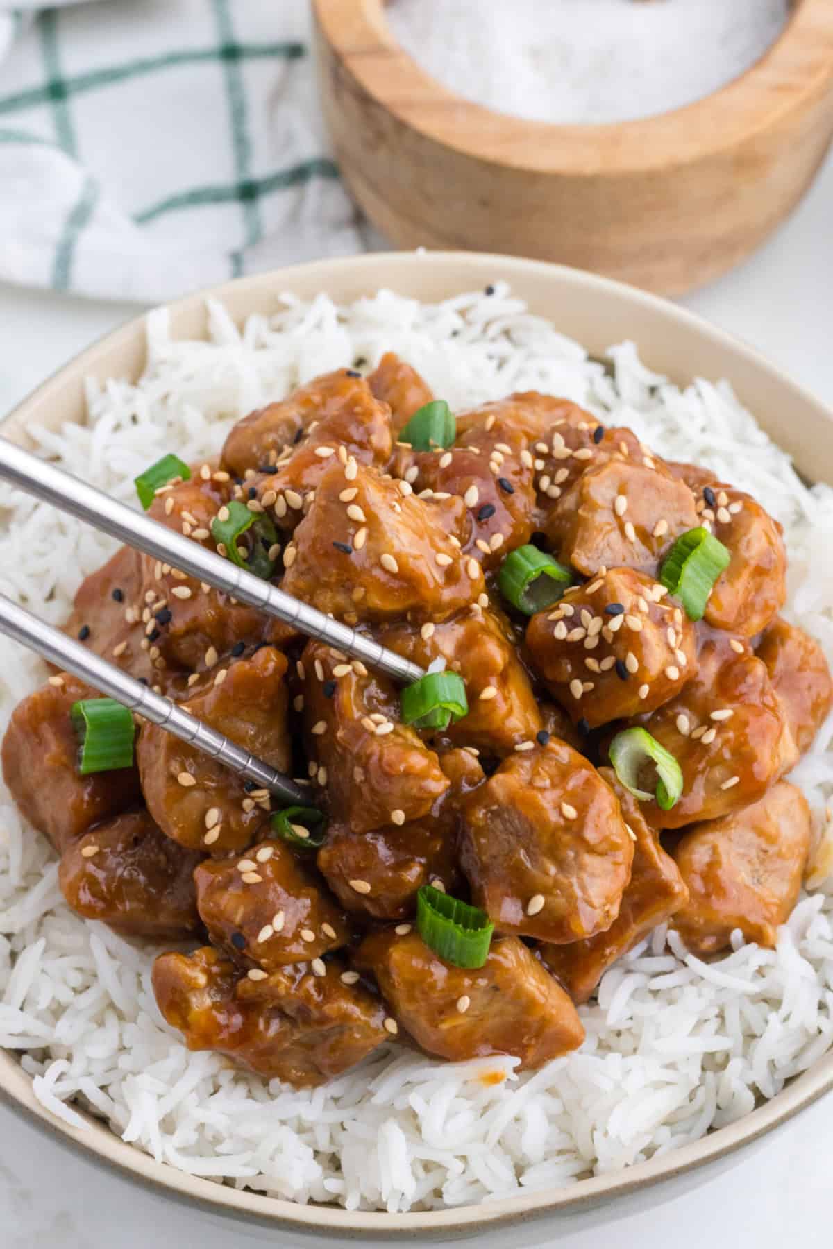 Asian Pork Tenderloin over rice in a bowl, with chopped green onion and sesame seeds on top.