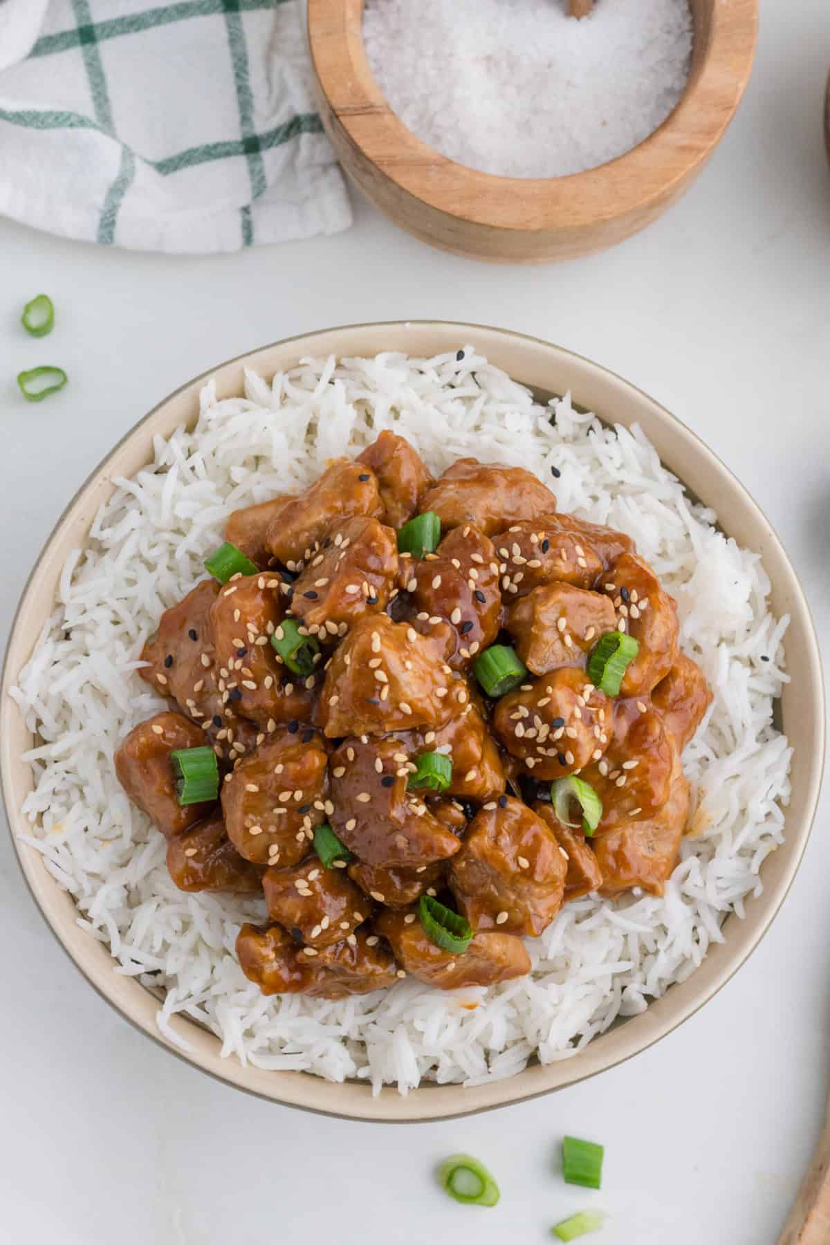 Asian Pork Tenderloin over rice in a bowl, with chopped green onion and sesame seeds on top.
