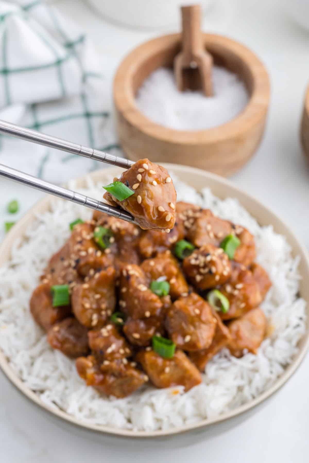 Chopsticks picking up a piece of asian pork tenderloin from a plate full with rice.
