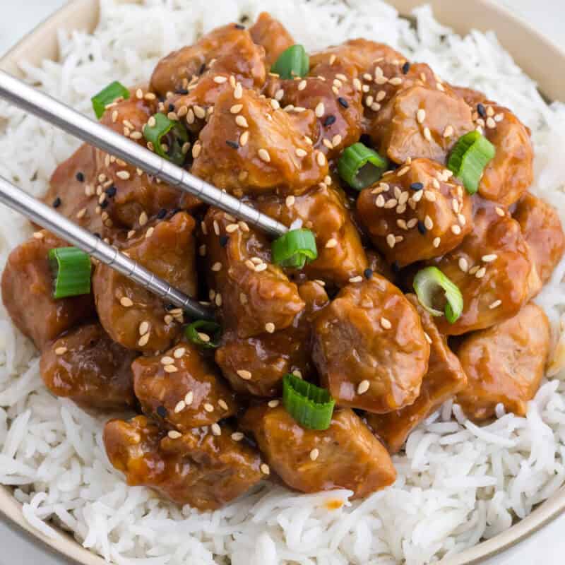 Asian Pork Tenderloin over rice in a bowl, with chopped green onion and sesame seeds on top.