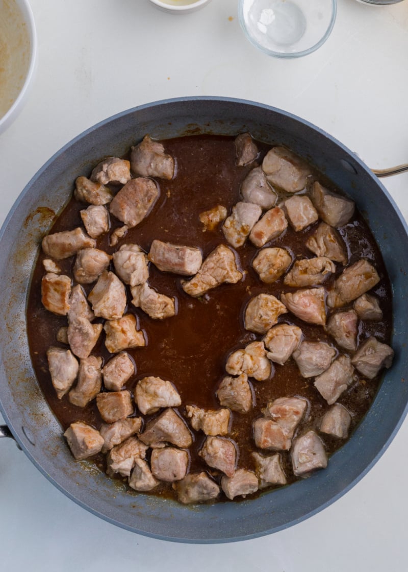 Cubed pork tenderloin cooking in a pan with sauce.