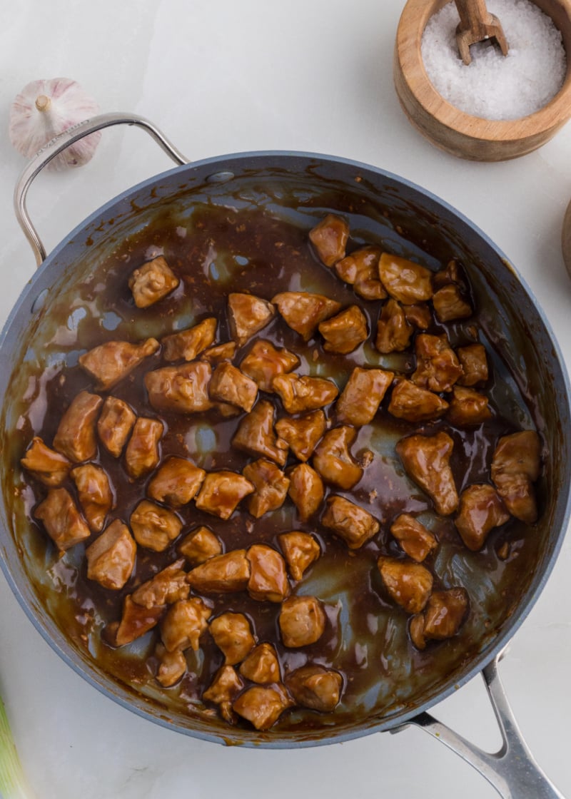 Cubed pork tenderloin cooking in a pan with a thick sauce.