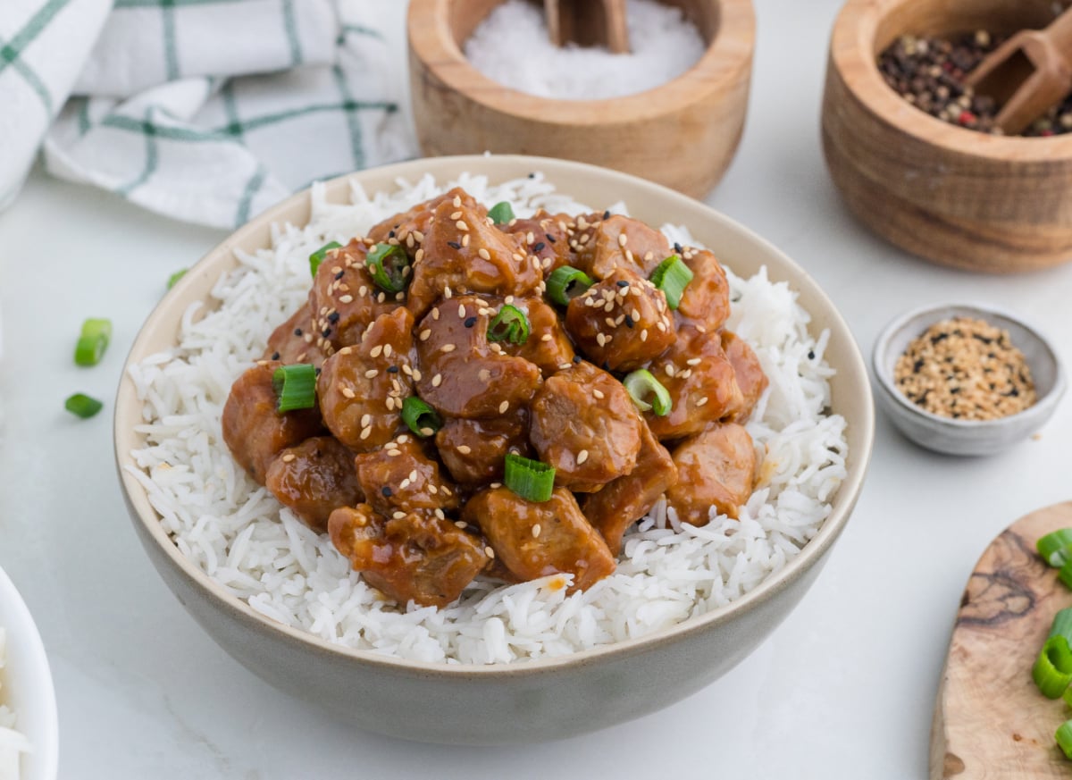 Asian Pork Tenderloin over rice in a bowl, with chopped green onion and sesame seeds on top.