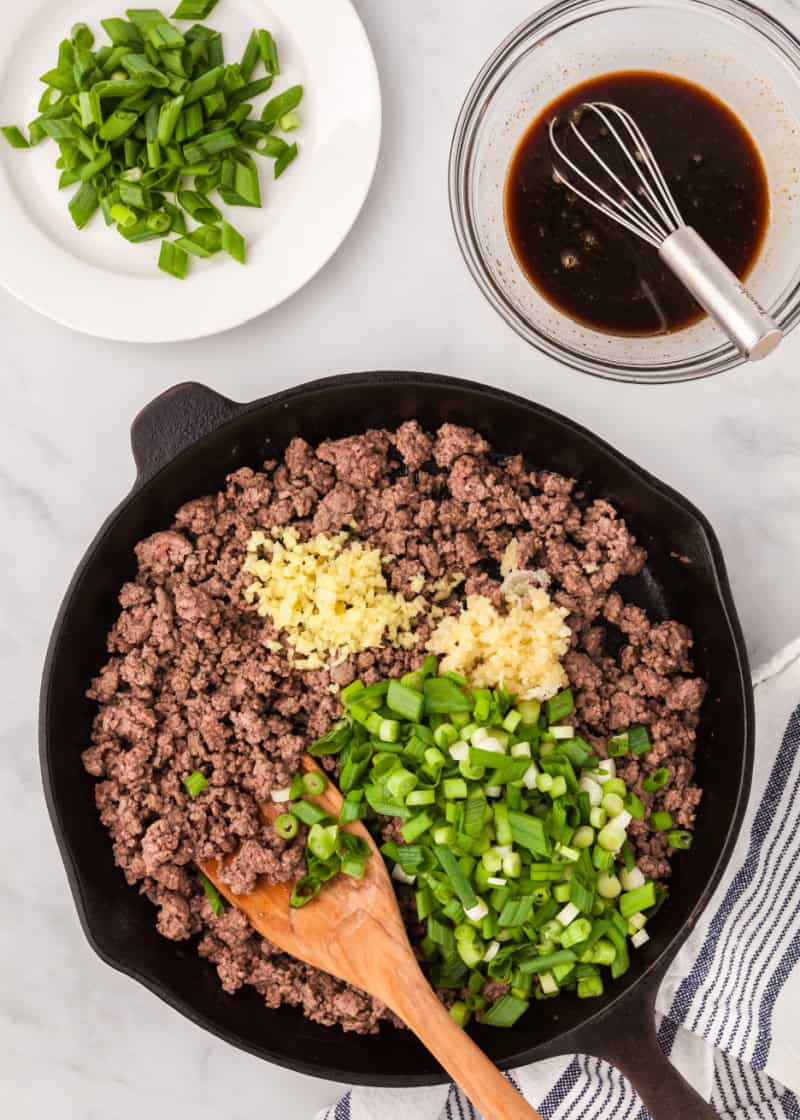 Korean ground beef being cooked in a black skillet with minced garlic and ginger.