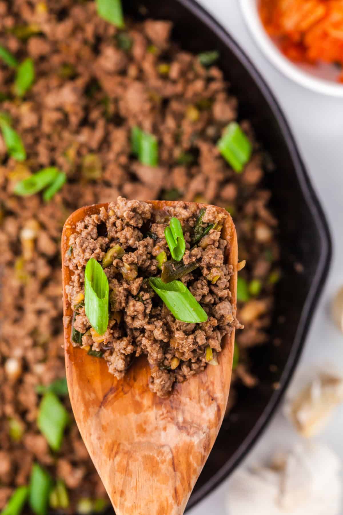 Korean ground beef on a wooden spoon over a pan.