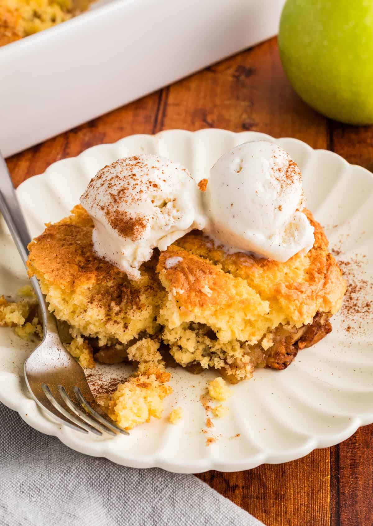 Cake Mix Apple Cobbler on a white plate with a fork, topped with two scoops of vanilla ice cream.