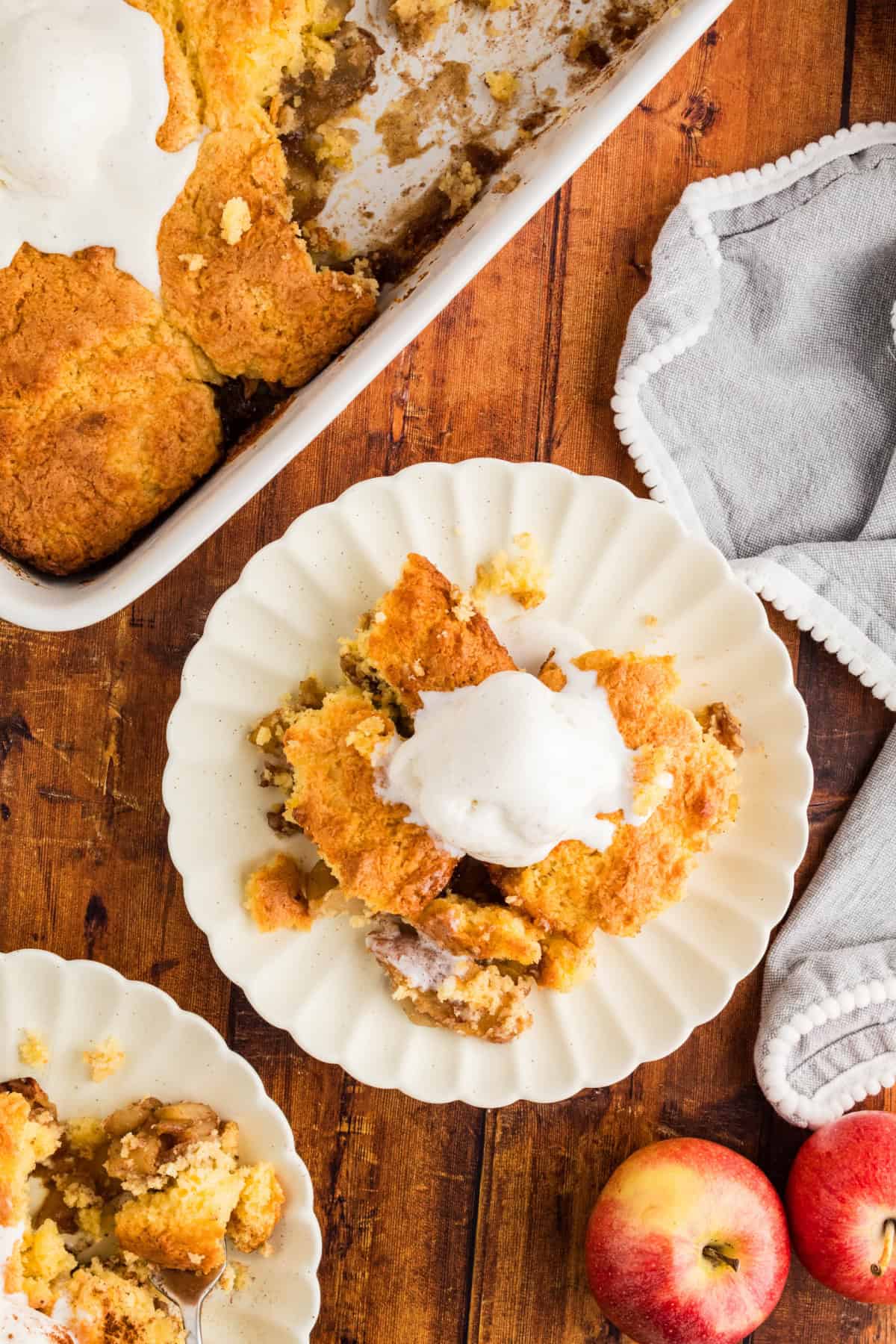 A baking tray of Cake Mix Apple Cobbler with ice cream, and two plates next to it.