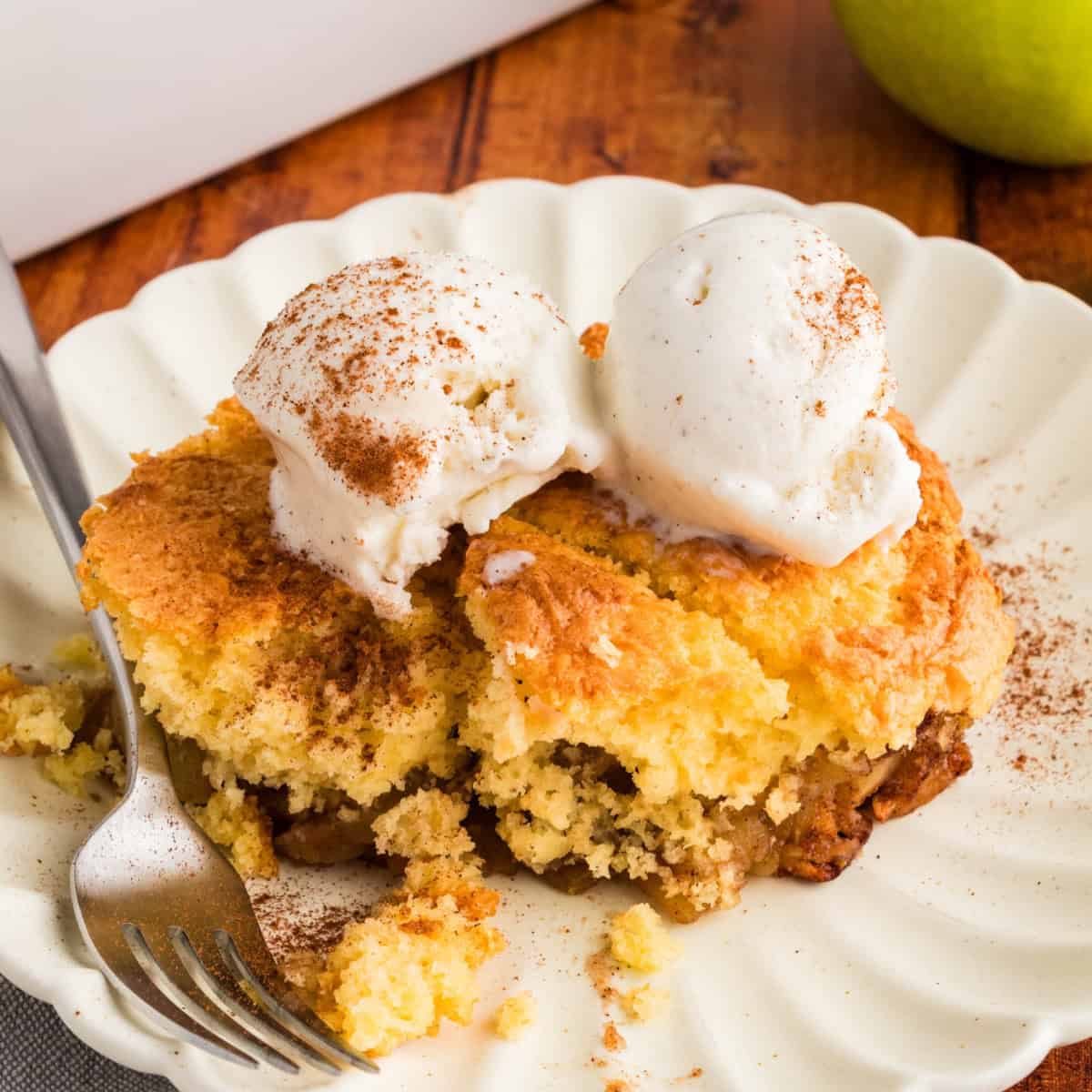 Cake Mix Apple Cobbler on a white plate with a fork, topped with two scoops of vanilla ice cream.