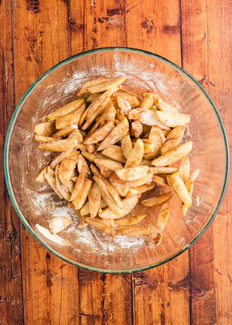 Sliced apples, dry cake mix, and spices in a glass bowl.