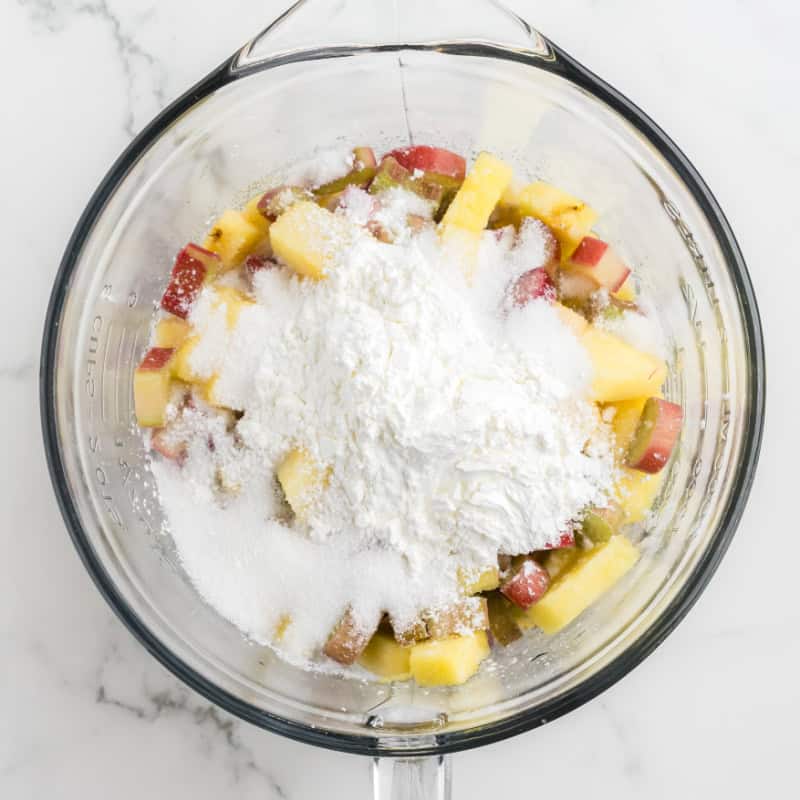 Pineapple and rhubarb chunks in a glass bowl with flour an baking powder.
