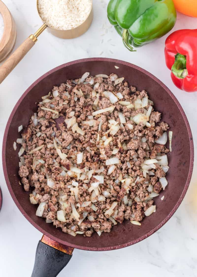 Cooked ground beef and chopped onion in a frying pan.