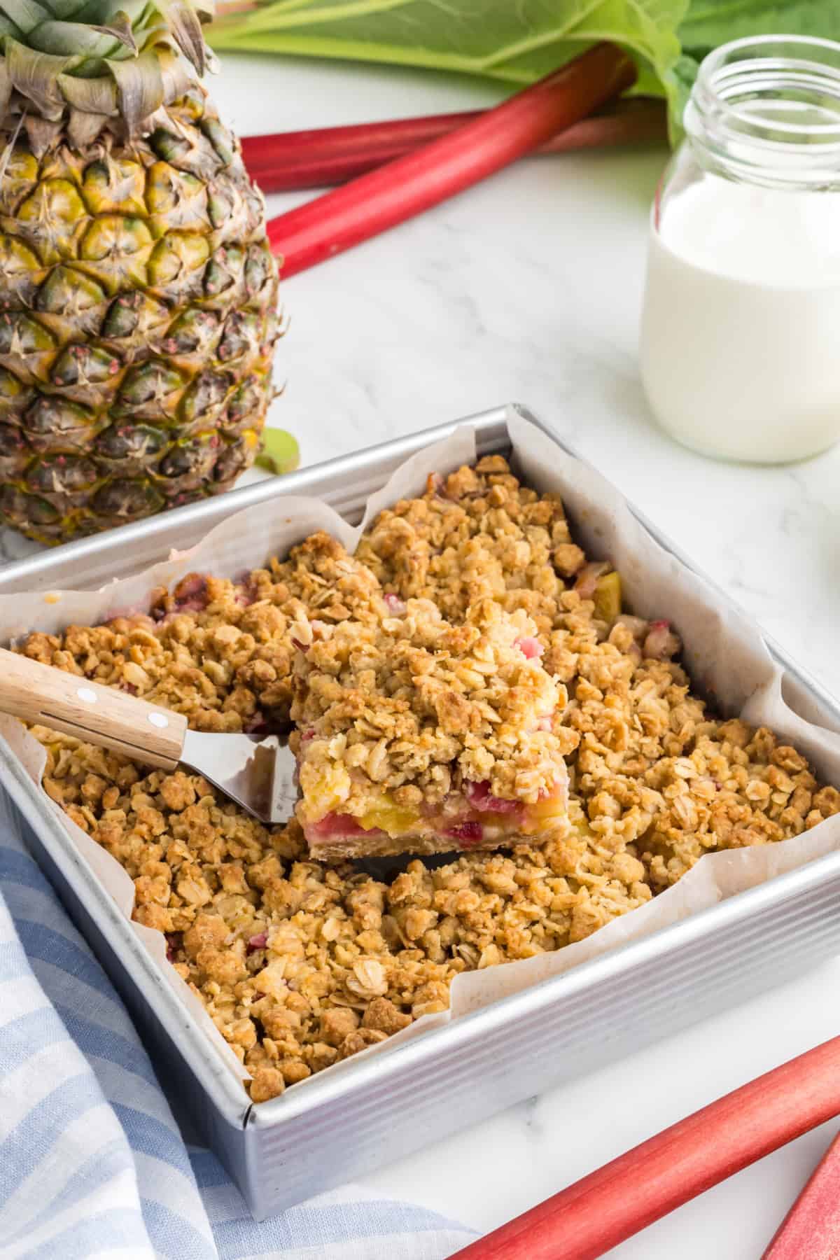 A slice of Pineapple Rhubarb Crumble Bar being lifted from a baking pan with a spatula.