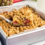 A slice of Pineapple Rhubarb squares being lifted from a baking pan with a spatula.