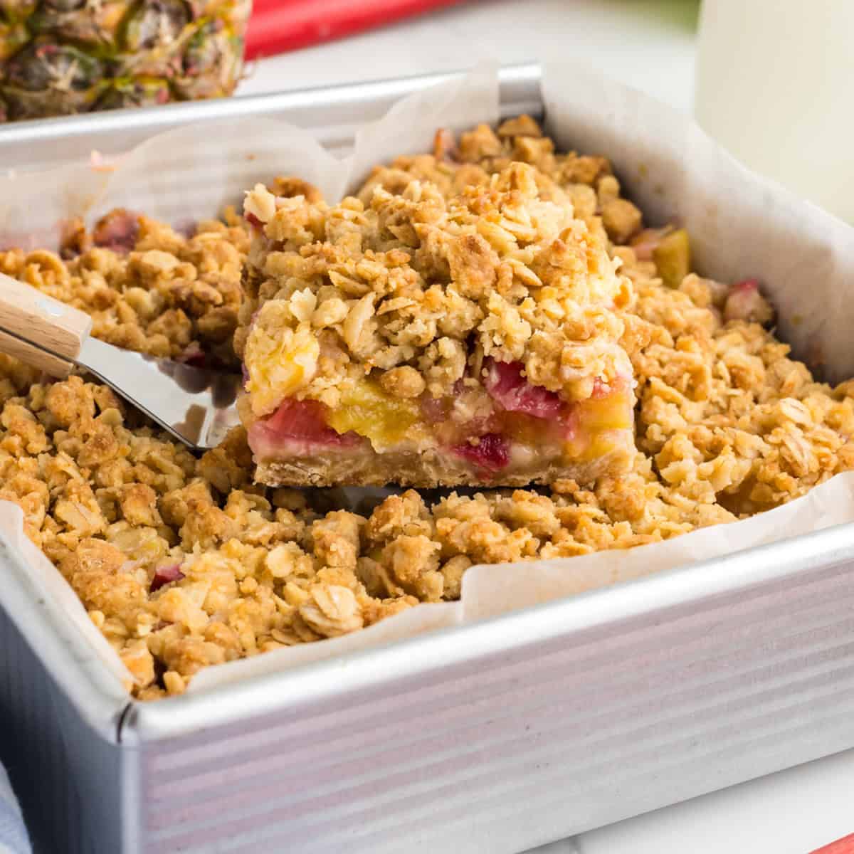 A slice of Pineapple Rhubarb squares being lifted from a baking pan with a spatula.